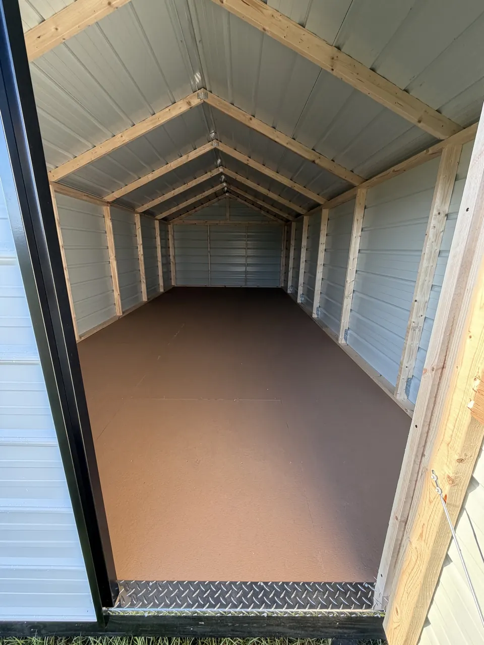 Inside an economy shed with metal walls, wood studs and rafters, and a diamond-plate threshold
